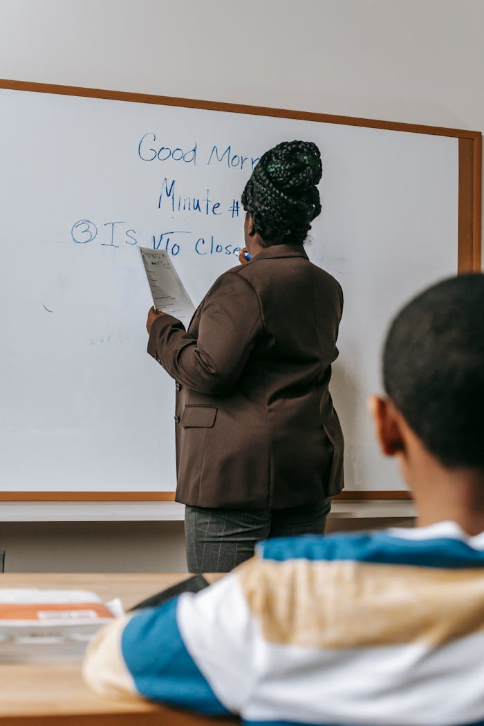 A teacher writes on a whiteboard during a classroom lesson, engaging with students.
