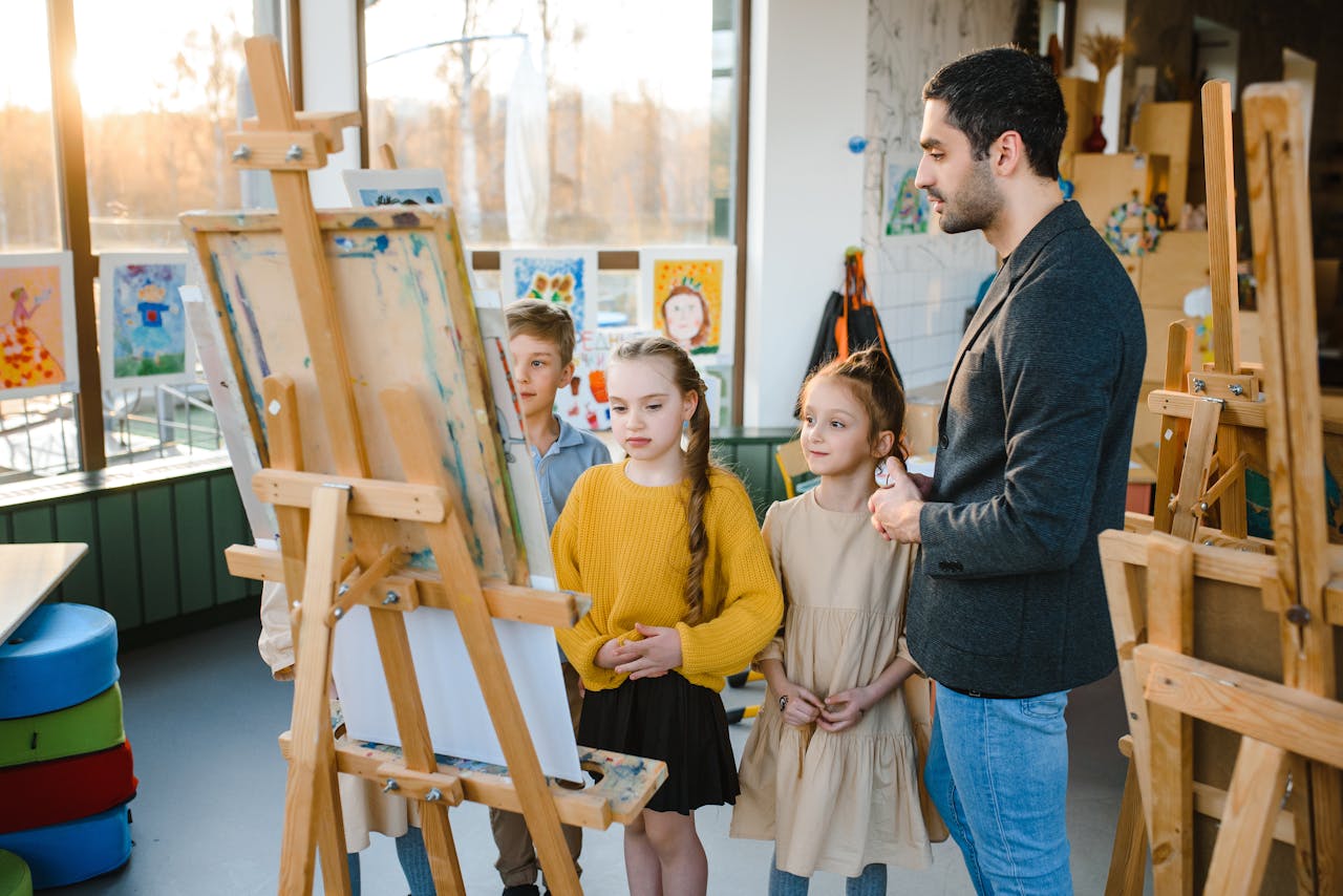 Children engaged in an art class under teacher's guidance, painting on easels.
